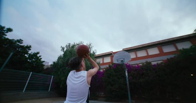 Basketball player shoot ball into hoop and keep focus on rim. Cinematic evening shot on outdoors court. Determination and hard work to achieve success. Eyes on target