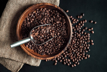 Coffee beans composition with metal scoop and burlap bag on dark background, top view. Stillife with heap of roasted Arabica grains in wooden bowl, decor for coffee shop. - 615752824