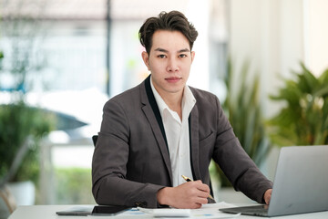 Portrait of businessman sitting at office desk, looking at camera.