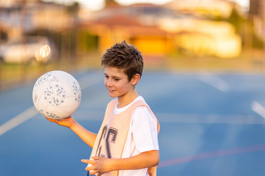 young boy wearing netball bib and holding ball on blue court