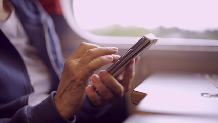 Close-up of the hands of an elderly woman sitting in a train carriageriage and using a smartphone