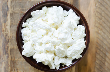 Organic cottage cheese in a brown ceramic bowl on a wooden background. The concept of homemade food. Top view. Horizontal orientation.