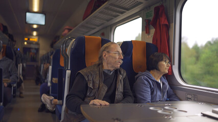 Elderly couple is riding in a train carriage and looking out the window