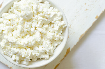 Organic cottage cheese in a white ceramic bowl on a light cutting board on a white tablecloth. Healthy breakfast. Concept of healthy food. Selective focus. Horizontal orientation. Top view