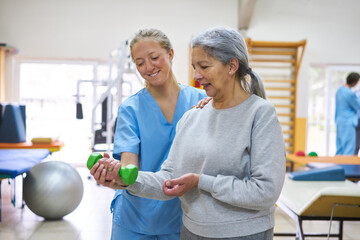 Nurse assisting senior woman exercising with dumbbell