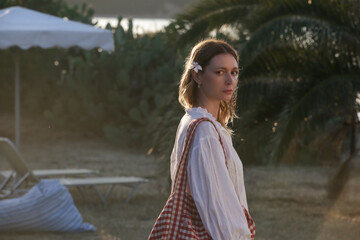 Portrait of young woman in linen blouse holding beach bag in the resort during summer vacation