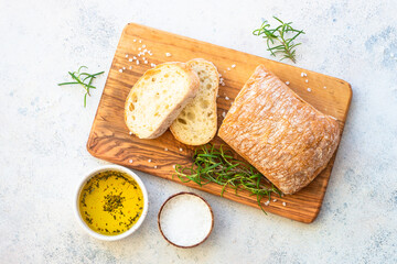 Ciabatta bread on wooden board with olive oil. Top view on white table.