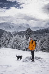 A person in a yellow coat and a black dog striking a pose amidst a picturesque snowy landscape, showcasing the beauty of their companionship.