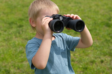 Little Boy using binoculars in a forest. 4 years kid looking ahead. Smiling kid with spyglass. Adventure, Imagination, travel concept. Freedom, vacation. Happy child playing outdoor in summer field