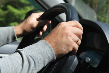 Male Hands holding steering wheel close up. Confident man driving a car during jorney trip. Side view from passenger inside car interior. Summer day. Driver. Selective Focus, Cropped. Travel concept