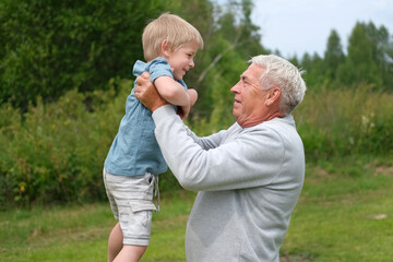 Grandfather and grandchild baby have fun during walk In Park. Happy family time. Old man grandpa hugging 4 years child boy at summer day. Smiling Senior male spending time with his grandson together.