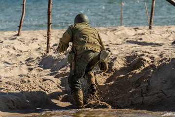 Historical reconstruction. An American infantry soldier from the World War II  fighting on the beach. Hel, Poland - obrazy, fototapety, plakaty