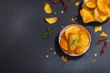 Bowls of homemade potato chips served with chili, parsley, seal salt on black stone background