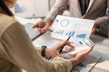 Team of two asian male and female business people working together discussing new financial graph data on office table with laptop and digital tablet.