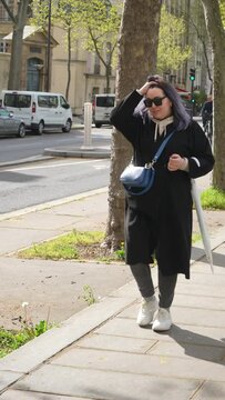 Vertical portrait of fashion plus size woman in coat walking along old Paris street on cold sunny spring day. Stylish female wearing sunglasses walking down Parisian street in springtime with umbrella