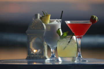 Pina colada, mojito and strawberry daiquiri cocktail glasses with beautiful sunset behind