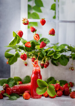 Fresh strawberry juice in a bottle surrounded by many fresh berries with splash and flying ingredients
