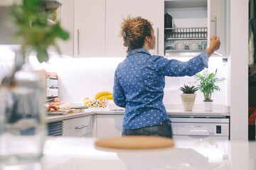 Back view of real life woman looking for in the kitchen living alone. Independent female people ready to prepare lunch at home. Copy space on left. One person busy in apartment.