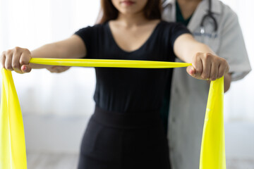 Doctor practicing arm and shoulder physiotherapy for female patient using latex therapy resistance band in exam room at hospital. Physical therapy and rehabilitation.