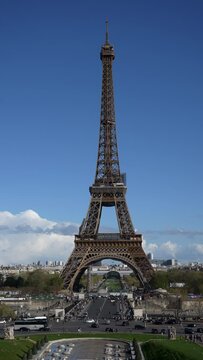 Remote vertical shot of Eiffel Tower on background blue sky on sunny day. Iconic symbol of Paris, famous historical landmark in France. Concept of vacations in France. Shooting in slow motion.