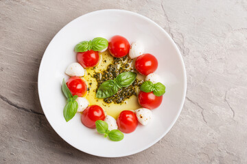 Caprese salad with tomato, mozzarella, basil, olive oil, pesto sauce on white plate on dark stone table. Mediterranean cuisine. Italian food. Top view.