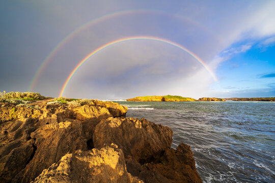 An intense double rainbow over a rocky coastline in morning sunshine