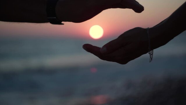 Red sun in twilight at sunset over Mediterranean sea with female and male hands making circle. Unrecognizable couple on ocean coast in dusk darkness. Romance and love concept