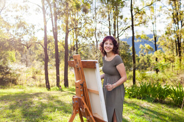 Smiling portrait of young australian artist standing beside canvas on easel