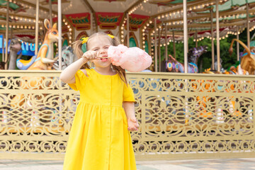 Little girl eating cotton candy in an amusement park. The concept of summer holidays and school holidays