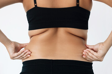 Fototapeta na wymiar Cropped shot of young woman standing with her back holds fat folds on her sides isolated on a white background. Overweight, flabby and sagging muscles, rolls on lower back. Excess weight