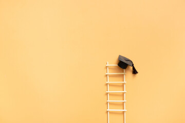 Graduation hat with ladder on an orange background with copy space © Alina
