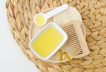 Small white bowl with honey, softgel capsules and wooden hairbrush. Natural skin and hair care,...