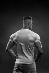 Athletic sexy man in white tight t-shirt posing in studio back view