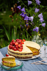 Homemade strawberry layered cake with vanilla custard on round table in blooming garden.