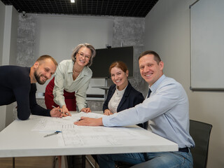 Designers engineers at a meeting discuss working drawings. Four smiling business people are looking at the camera.