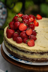 Fresh strawberries on top of homemade sponge cake with custard on wooden cake stand  in blooming garden.