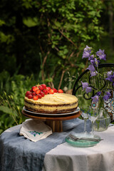 Homemade strawberry cake on wooden cake stand on round table in blooming garden.
