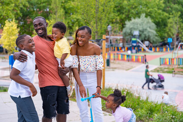 African black ethnicity family having fun with happy children together in playground, greeting each...