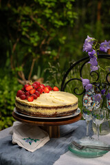 Homemade strawberry cake on wooden cake stand on round table in blooming garden.