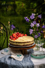 Midsummer homemade strawberry cake on wooden cake stand on round table in blooming garden.