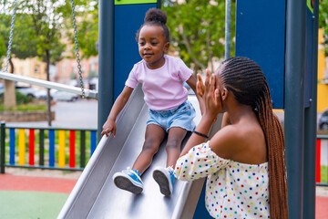 African black ethnicity mother having fun with her daughter in the squeaker of the playground of...