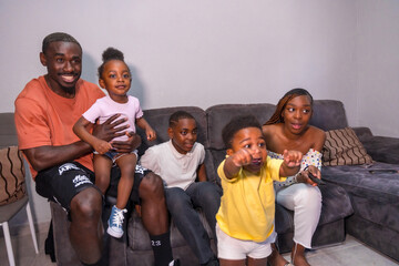 Portrait of black African ethnicity family with children on the sofa at home having fun watching TV