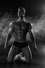 Muscular shirtless man with perfect body posing kneeling in studio