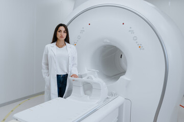 A young female doctor stands next to a magnetic resonance imaging machine. Diagnostic room in the medical center.
