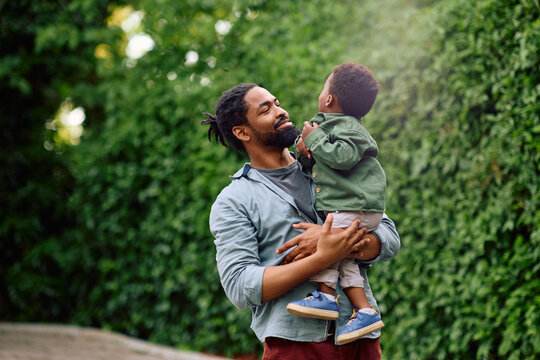 Happy black father carrying his small son while walking in park.