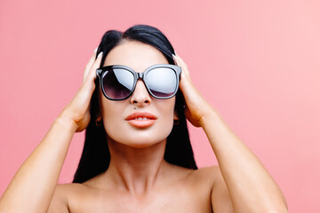 Sexy woman in black swimsuit with sunglasses isolated on pink background in studio.