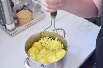 Person prepares mashed potatoes. Crushed potatoes in a saucepan.