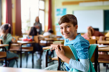 Happy schoolboy attending class in classroom and looking at camera.