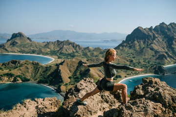 A beautiful young girl doing yoga on top of a mountain overlooking Padar Island, Indonesia.
