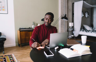 Concentrated black man taking notes during work